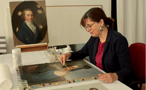 Diplom-Restauratorin Maike Behrends bei der Arbeit an Luise Seidlers Porträt der Ottilie Arnoldi, im Hintergrund J.F.A. Tischbeins Porträt Hufelands, © Maike Behrens