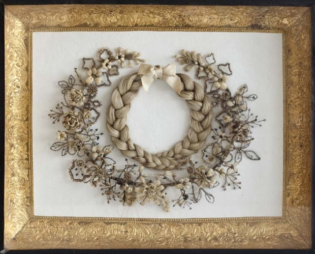 Kranzkasten, 1900, stilisierter Blütenkranz aus Haaren mit hinein gelegten geflochtenen Zöpfen Wem dieses Gedenkbild gewidmet wurde, ist unbekannt. Es wird vermutet, dass es sich um ein verstorbenes Kind der (Groß-)mutter der Stifterin handelt, Foto: Museum für Sepulkralkultur, Kassel